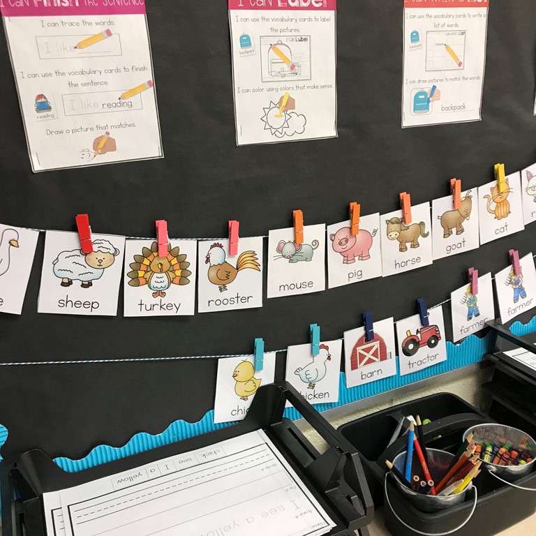 Setting up your writing center supplies [picture shows I can posters, writing center vocabulary cards attached to a string with clothespins, and writing center activities on trays]