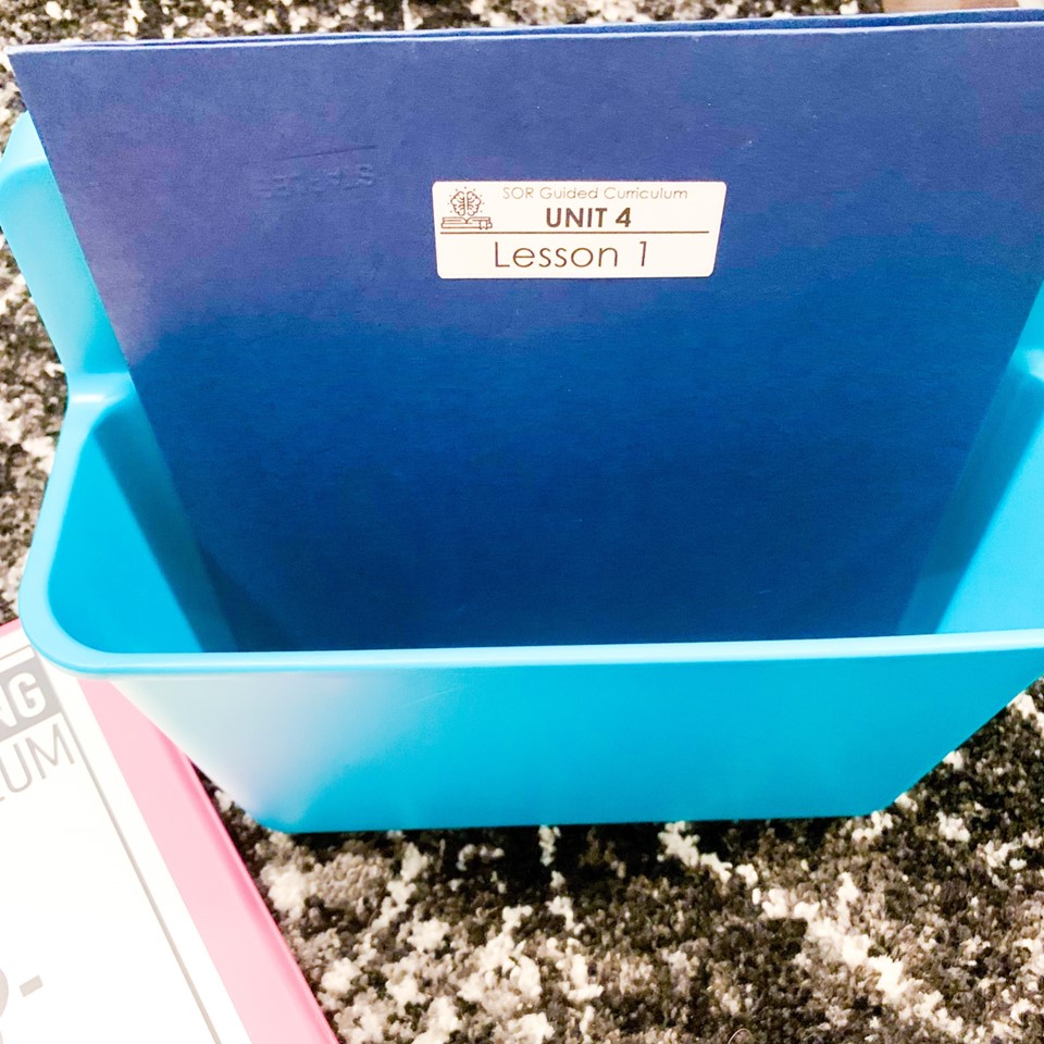 Organized Science of Reading Guided Curriculum materials in a paper folder stored in a plastic tub