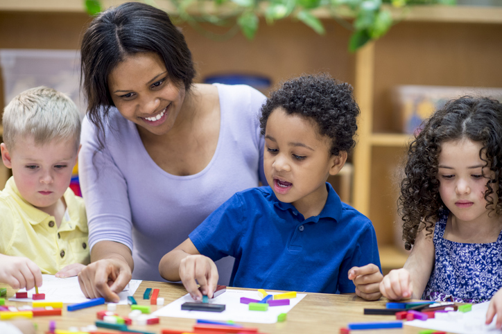 image shows a teacher sitting with 3 children who are using cuisinare rods